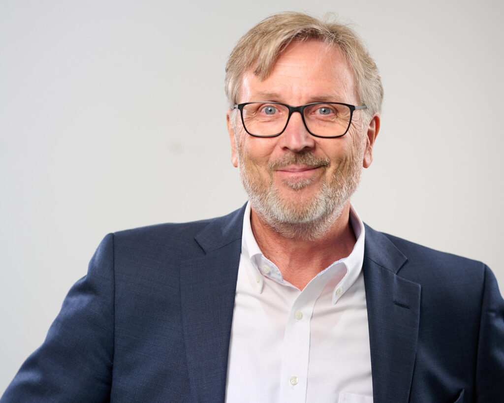 Das bild zeigt Jens Kellersmann, lächelnd in weißem Oberhemd und blauem Sakko.